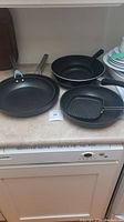 Four fry pans on kitchen countertop including three round pans and one square grill pan.