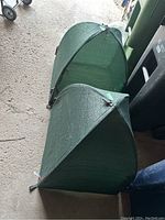 Two green mesh fabric hedge protectors with triangular structure placed on the ground.