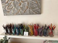 Wide angle showing 10 glass jars filled with assorted colored pencils arranged by color.