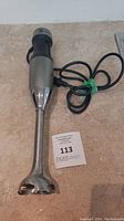 Full length view of immersion hand blender including blade guard, shaft, handle with button, and attached power cord.