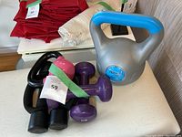Photo showing the 10 lb silver-blue kettlebell, 5 lb black kettlebell with pink top, purple 5 lb dumbbells, and other free weights.