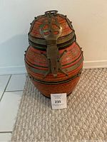 Front view of the painted wooden urn showing the red-orange floral patterns and brass hardware.