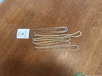 Five pearl necklaces laid out on a wooden surface showing the variety in size and color of pearls with metal clasps visible.