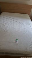 Queen size bedframe with mattress and fitted sheet on it, showing headboard and mattress surface with auction tag.