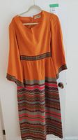 Full view of the orange vintage dress with patterned trim on sleeves, waist, and skirt.