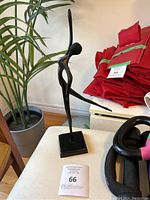 Side angle view of the vintage Ikea Bodrul Khalique black dancing ballerina sculpture figurine on a small table with a plant in the background.