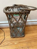 Side view of wicker basket with square heavy glass candle holder inside, showing basket weave and handle.