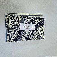 Folded navy blue and cream paisley patterned tablecloth with a MaxSold tag on white quilted surface.
