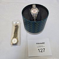 Two women's watches shown together: Relic watch in a round box and Orkina watch in plastic packaging.