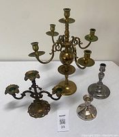 Front view of all four items: large brass candelabra, smaller brass candelabra, silver candlestick and pewter candlestick.