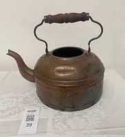 Antique copper gooseneck kettle with wooden handle, showing tarnish and dents.