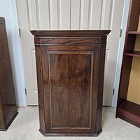 Front view of antique mahogany corner cabinet with closed door and visible wood grain.