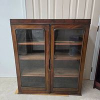 Front view of closed antique mahogany cabinet with glass double doors, showing wood grain and door frames.