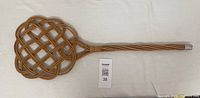 Full view of antique woven rattan rug beater showing metal-covered handle end.