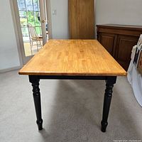 Front view of solid wood table with natural wood finish top and black turned legs.