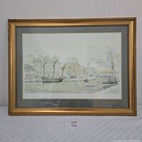 Framed print showing entire artwork in gold frame with mat border, depicting boats and buildings along a French coastal town.