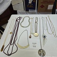Overview of all jewellery laid out on a white sheet including beaded, gold-tone and silver-tone necklaces and pendants.