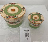 Top view of two vintage ceramic canisters with lids and floral designs, one large and one small, showing the wood knobs on lids.