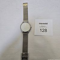 Top-down view of men's watch showing full length of stainless steel mesh strap and round face on white background.