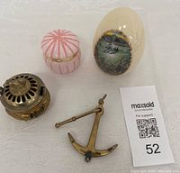Photo of all four items on white cloth background: brass anchor, alabaster jewelry box, porcelain dolphin egg, vintage incense burner
