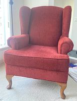 Front view of dark rusty-red wingback armchair showing seat cushion, armrests, and wooden cabriole legs.