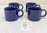 Four large, deep cobalt blue ceramic mugs arranged on a light surface, showing the side and handle profile of the mugs.