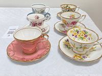 Set of six vintage china tea cups with matching saucers displayed diagonally with varied floral patterns and gold trim.