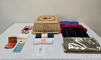 Full bulk lot showing vintage sewing box with needlepoint lid, fabric pieces, and sewing supplies arranged on a table.