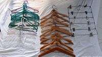 Photo showing a collection of 30 hangers including 12 wooden vintage style hangers, 11 colored plastic hangers, 4 clear plastic hangers, 2 cloth-covered hangers, and 1 large metal multi-item hanger with clips.