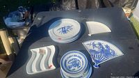 Photo of Asian plates and dishes including round plates with blue designs, fan-shaped plates, and a three-section serving dish on a black table outdoors.
