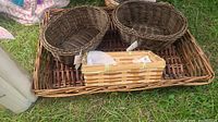 Four bamboo baskets placed on grass, showing a large flat tray base, two round baskets and one rectangular basket with hinged lid