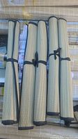Four rolled beige woven beach mats tied with black fabric strips, displayed side by side.