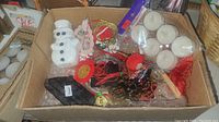Photo of a box filled with Christmas-themed candles and ornaments, including a ceramic snowman and tea light candles