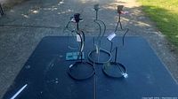 Four decorative metal candle holders of varying shapes and colors arranged on an outdoor black table in sunlight, showing condition and design details.