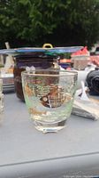 Photo of a clear glass tumbler with a shiny fish design displayed on an outdoor table among miscellaneous items.