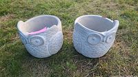 Two owl-shaped concrete garden pots placed on grass, showing texture and condition.