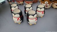 Photo showing six black and white ceramic holders shaped like penguins with red scarves, hollow in center.