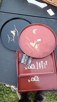 Four plastic Japanese trays displayed: two round trays with gold designs (birds and rabbit) and two rectangular trays with Japanese calligraphy and face illustrations.