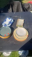 Photo showing multiple stacks of plates including round beige and green plates and stacks of blue and white square patterned plates.