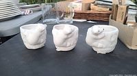 Three white ceramic holders shaped like polar bears displayed on a dark surface outdoors. The bears are detailed with different poses and smooth finish.