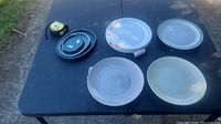 Five round ceramic plates displayed on a black surface outdoors along with a measuring tape and a small container.