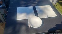 Two white square plates and one white round bowl placed on a black surface outdoors