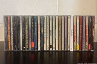Photo shows 22 music CDs lined up, titles and artists visible on the spines.