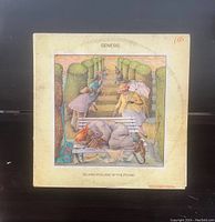 Photo showing the front cover of the vinyl LP album "Selling England By The Pound" by Genesis. The cover art features a distinct garden scene with multiple figures and a bench.