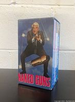 Front view of the Naked Guns VHS box set featuring a man holding a gun with bullet graphics on blue background.
