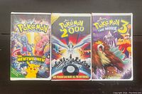 Photo of three original Pokémon VHS tapes: The First Movie, Pokémon 2000, and The Movie 3 with bright colorful covers showing iconic Pokémon characters.