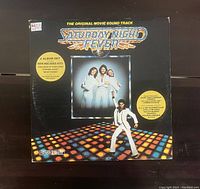 Front cover of the Saturday Night Fever original soundtrack 2 vinyl album set, featuring disco themed artwork and cast photos.