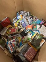 Photo of a large bin filled with assorted books and DVDs in various conditions but generally very good. Visible book topics include gardening, curriculum, cooking, and others. DVDs appear to be a mix of movies and TV series.