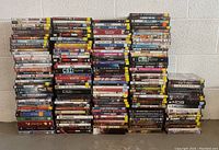 Large assortment of DVDs stacked in tall piles on the floor. Shows mix of movie and TV series DVDs with visible titles such as The Guardian, Justice Savage, NCIS, CSI and others.