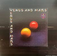 Front cover of the Wings album "Venus And Mars" vinyl record, showing original artwork with colorful letters and two spheres.